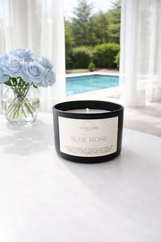 Candle labeled 'Blue Rose' on a table with a pool and garden view in the background