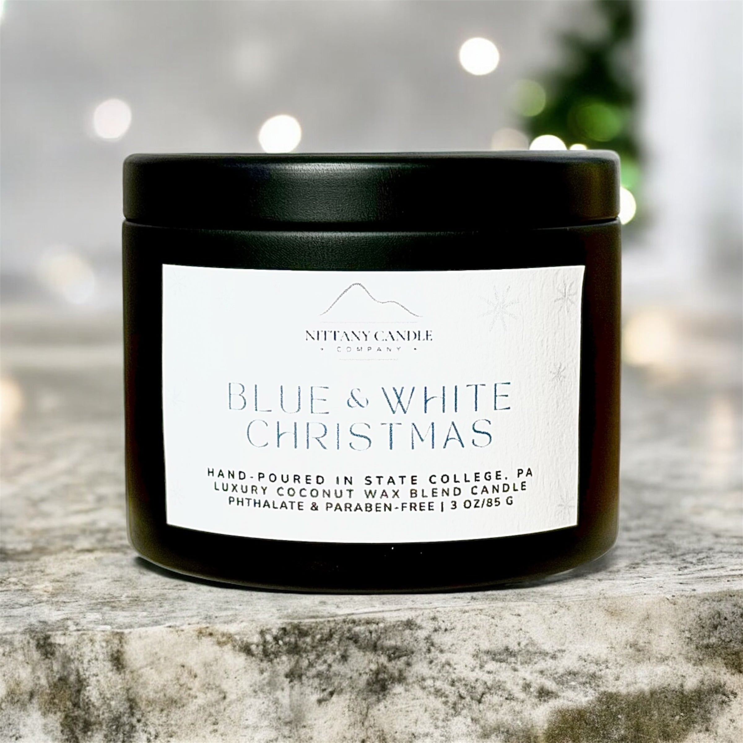 Nittany Candle Company candle with a Penn State themed label on a stone surface with blurred Christmas lights in the background