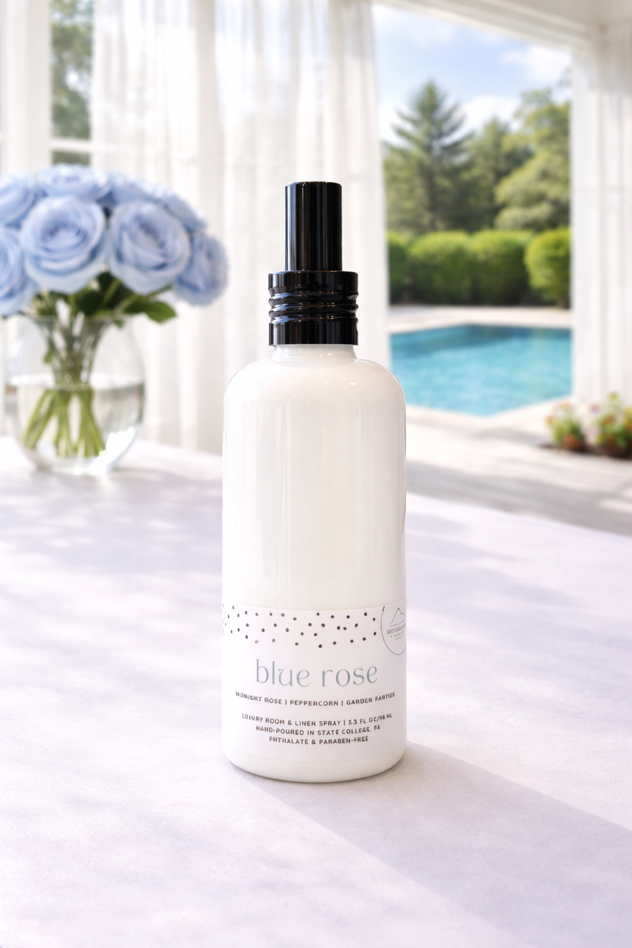 Blue Rose Penn State Themed Linen Spray on a white table with blue roses and a pool in the background