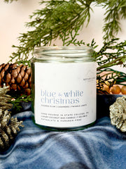 Penn State themed candle jar labeled 'Blue & White Christmas' surrounded by pine cones and branches on a textured surface.