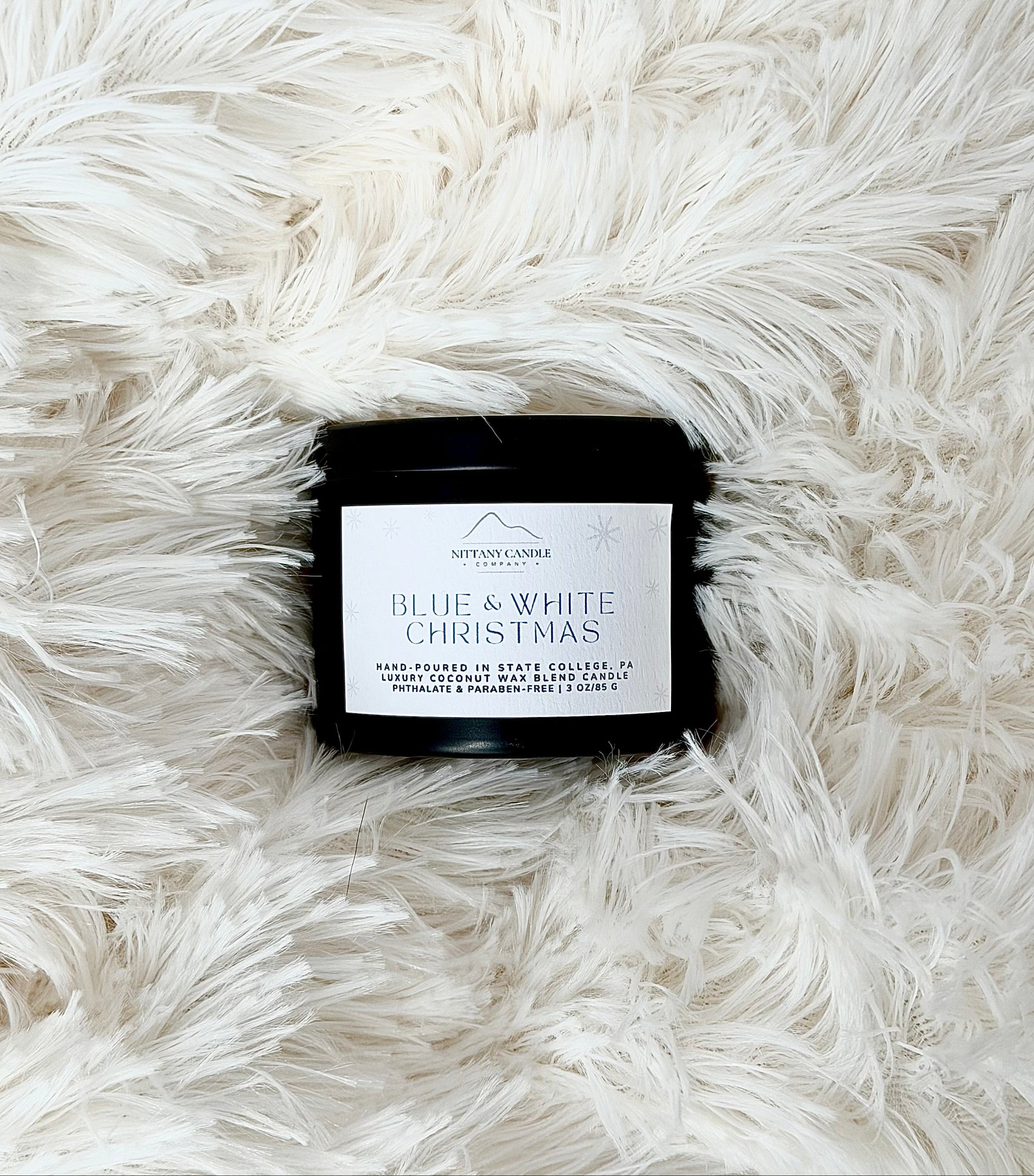 Small Penn State themed candle labeled 'Blue & White Christmas' on a white fluffy surface