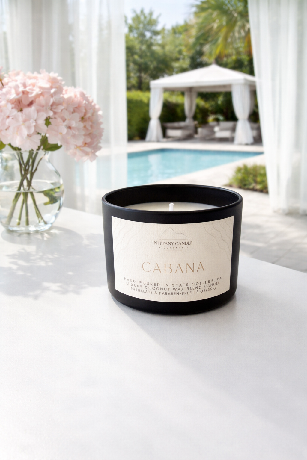 Nittany Candle Company 'cabana' candle on a white table with a pool and cabana in the background