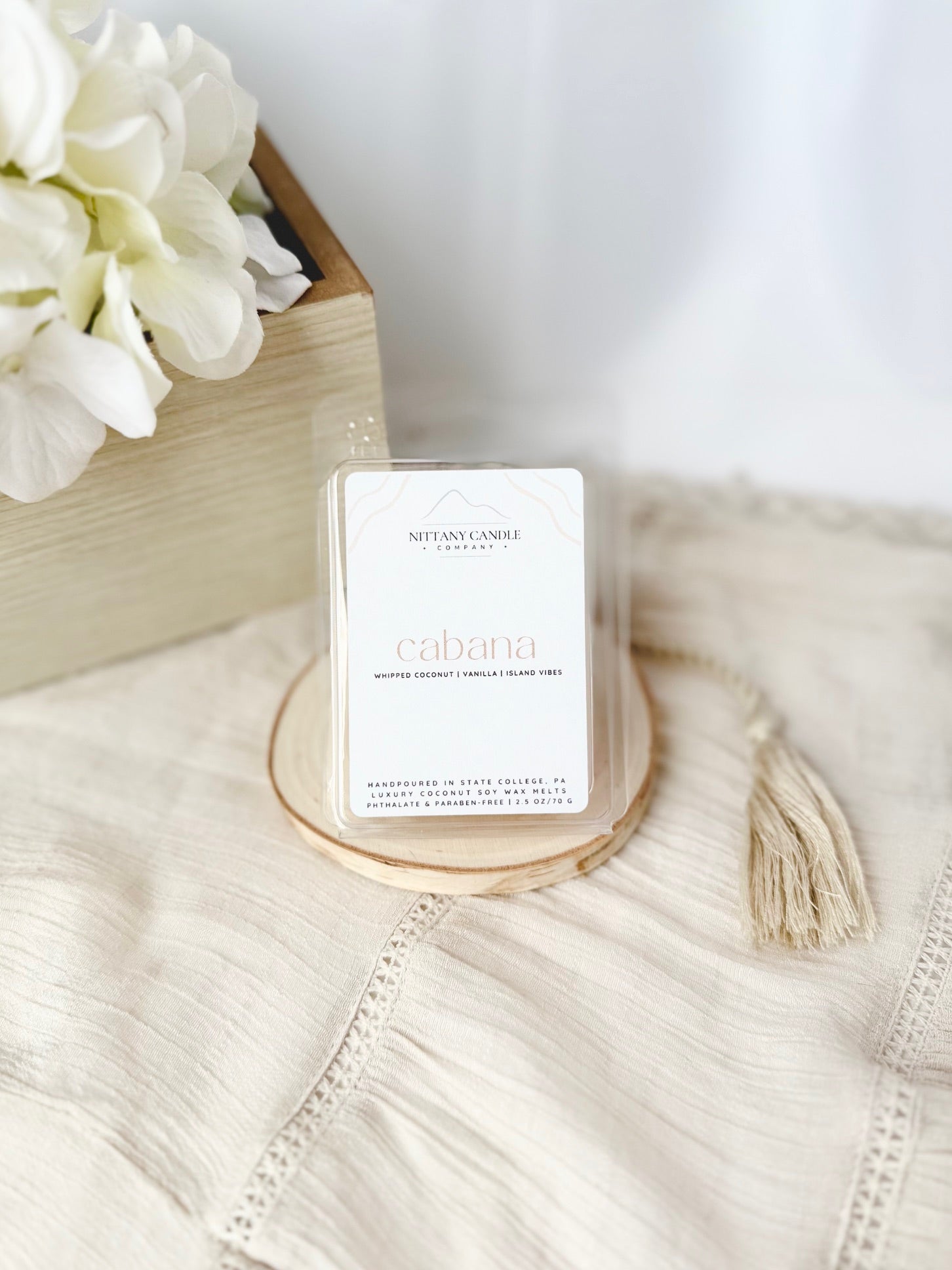 Candle labeled 'cabana' on a textured surface with white flowers in the background