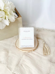 Candle labeled 'cabana' on a textured surface with white flowers in the background