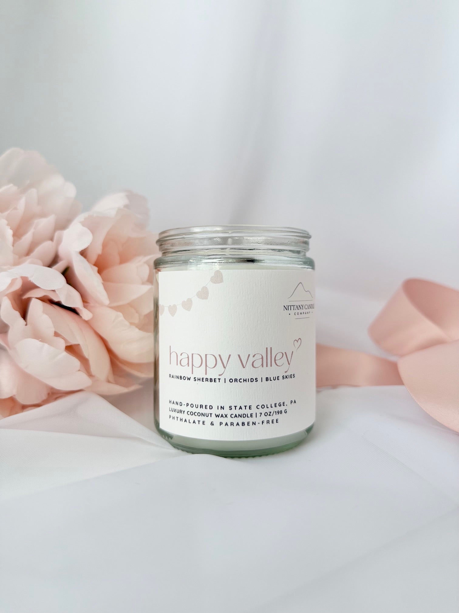 Candle jar labeled 'happy valley' with pink flowers in the background