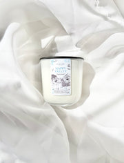A white scented candle with a black lid and a white label reading 'Happy Valley,' styled on draped white fabric.