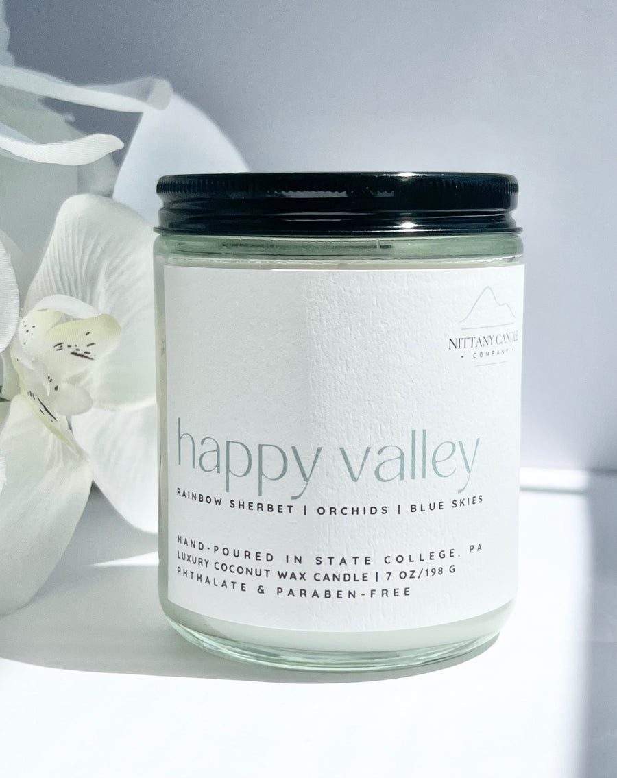 Penn State gift candle jar labeled 'happy valley' with a white orchid in the background