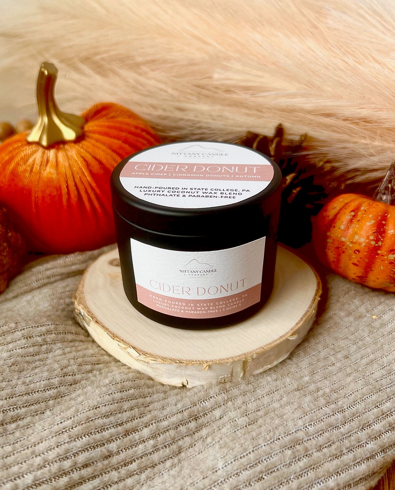 Cider Donut candle on a wooden coaster with pumpkins in the background