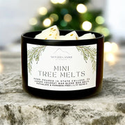 Black container of mini tree melts with a label on a wooden surface, Christmas tree in the background