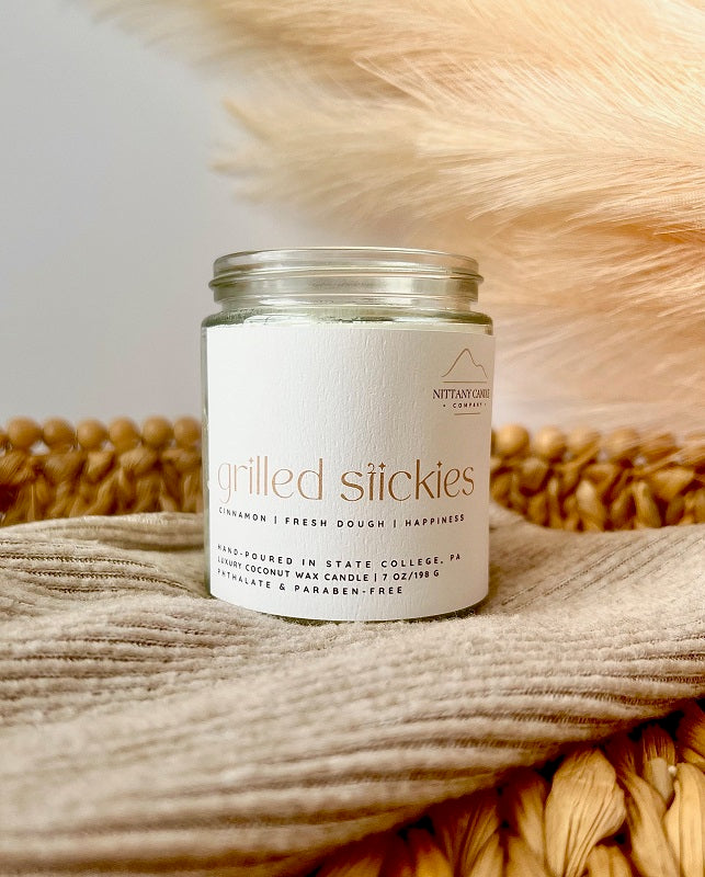 Nittany Candle Company candle jar labeled 'Grilled Stickies' on a textured surface with a neutral background