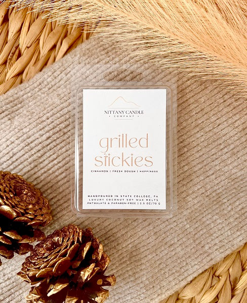 Nittany Candle Company wax melt package labeled 'Grilled Stickies' on a textured surface with pinecones.