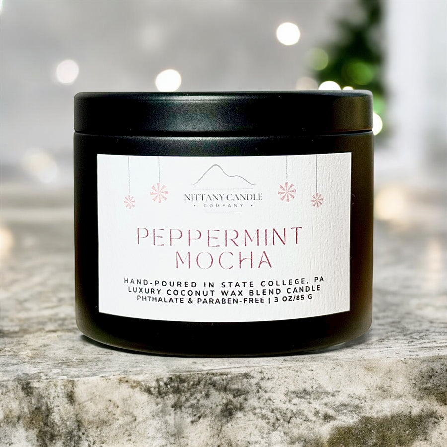 Black candle with 'Nittany Candle Company' label on a marble surface with blurred lights in the background