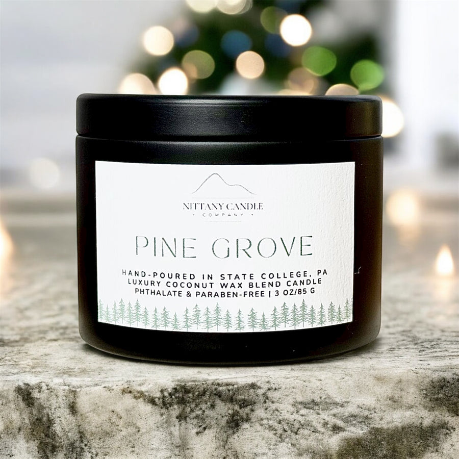Candle labeled 'Pine Grove' by Nittany Candle Co. on a wooden surface with a blurred background of lights.