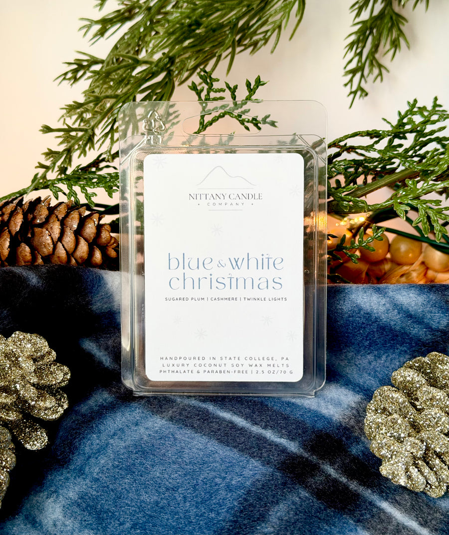 Nittany Candle Company Penn State-themed wax melt packaging with Christmas decor on a blue fabric background.