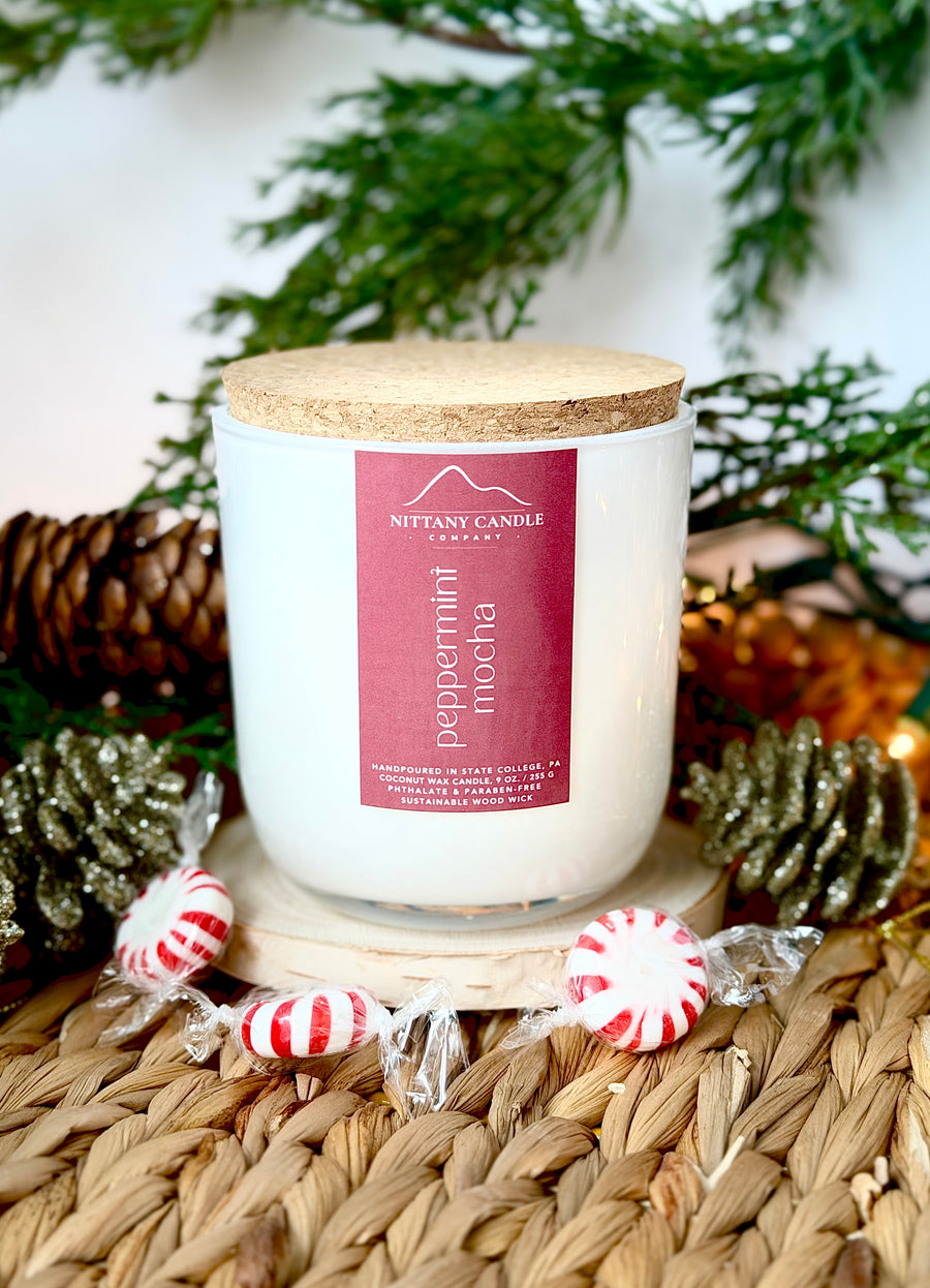 Wood wick candle with peppermint mocha label on a woven surface with Christmas decorations