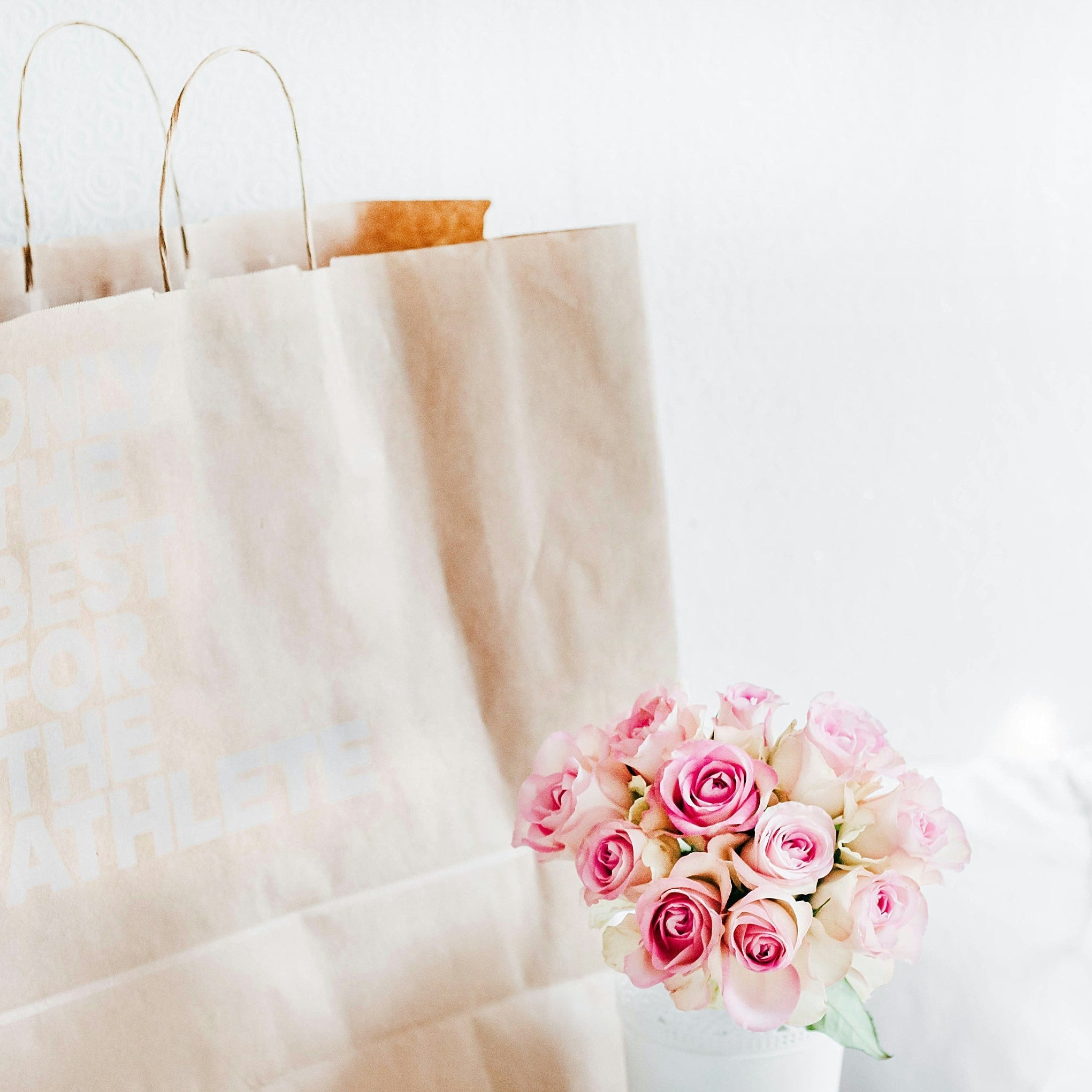 Brown paper bag with a bouquet of pink roses on a white surface
