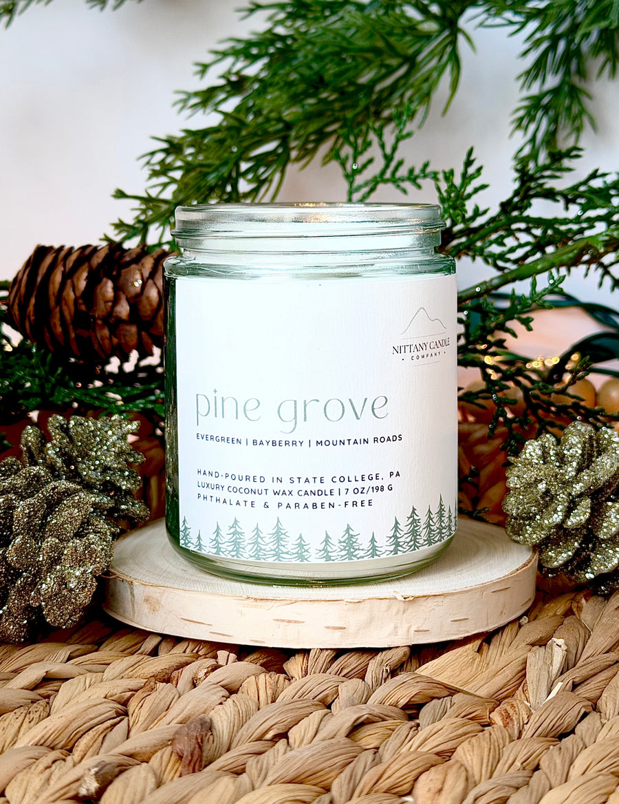 Nittany Candle Company candle labeled 'Pine Grove' on a woven surface with decorative elements.