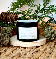 Candle labeled 'Pine Grove' surrounded by decorative pinecones and branches on a woven surface.