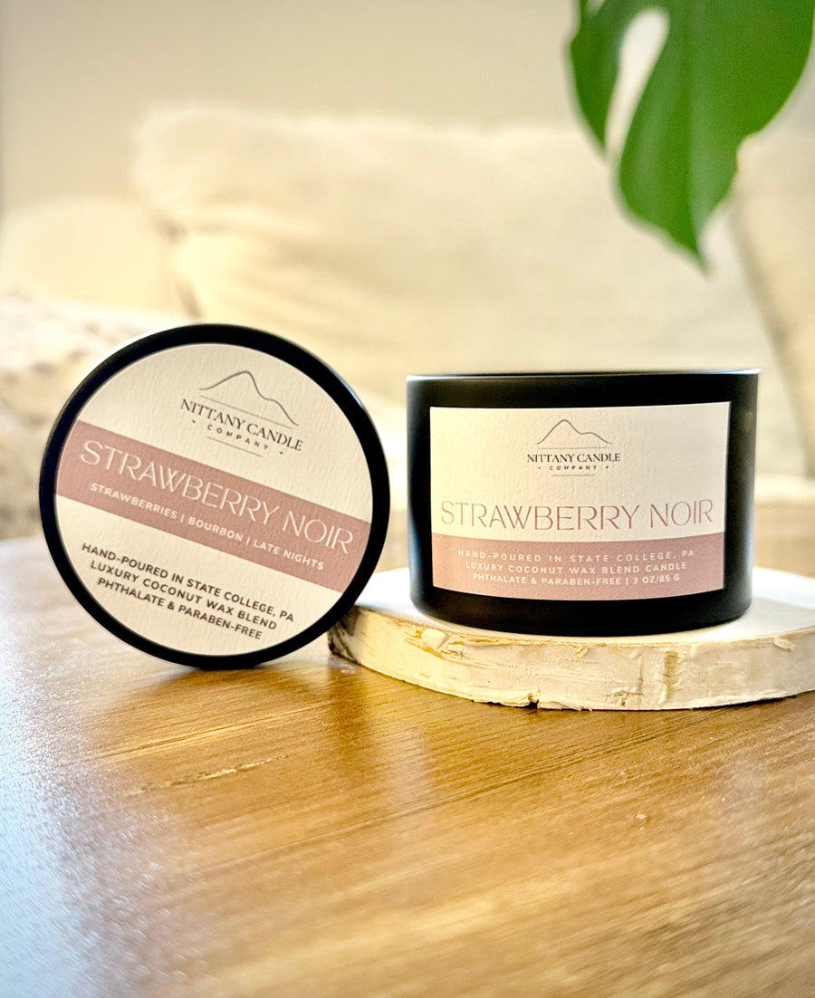 Two candles labeled 'Strawberry Noir' by Nittany Candle Company on a wooden surface.
