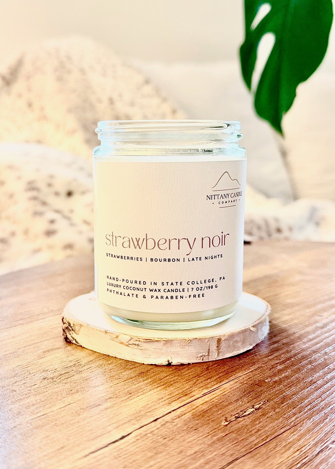 Candle labeled 'strawberry noir' on a wooden coaster with a blurred background