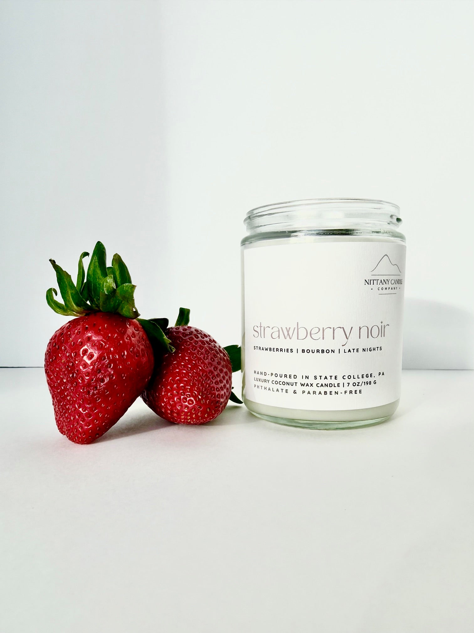 Candle labeled 'Strawberry Noir' next to two strawberries on a white background