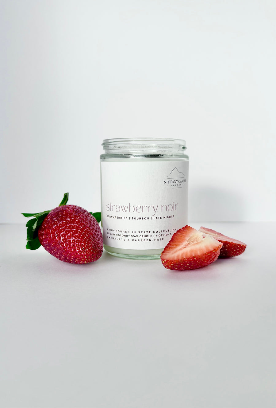 Nittany Candle Co candle jar of 'Strawberry Noir' candle with strawberries on a white background