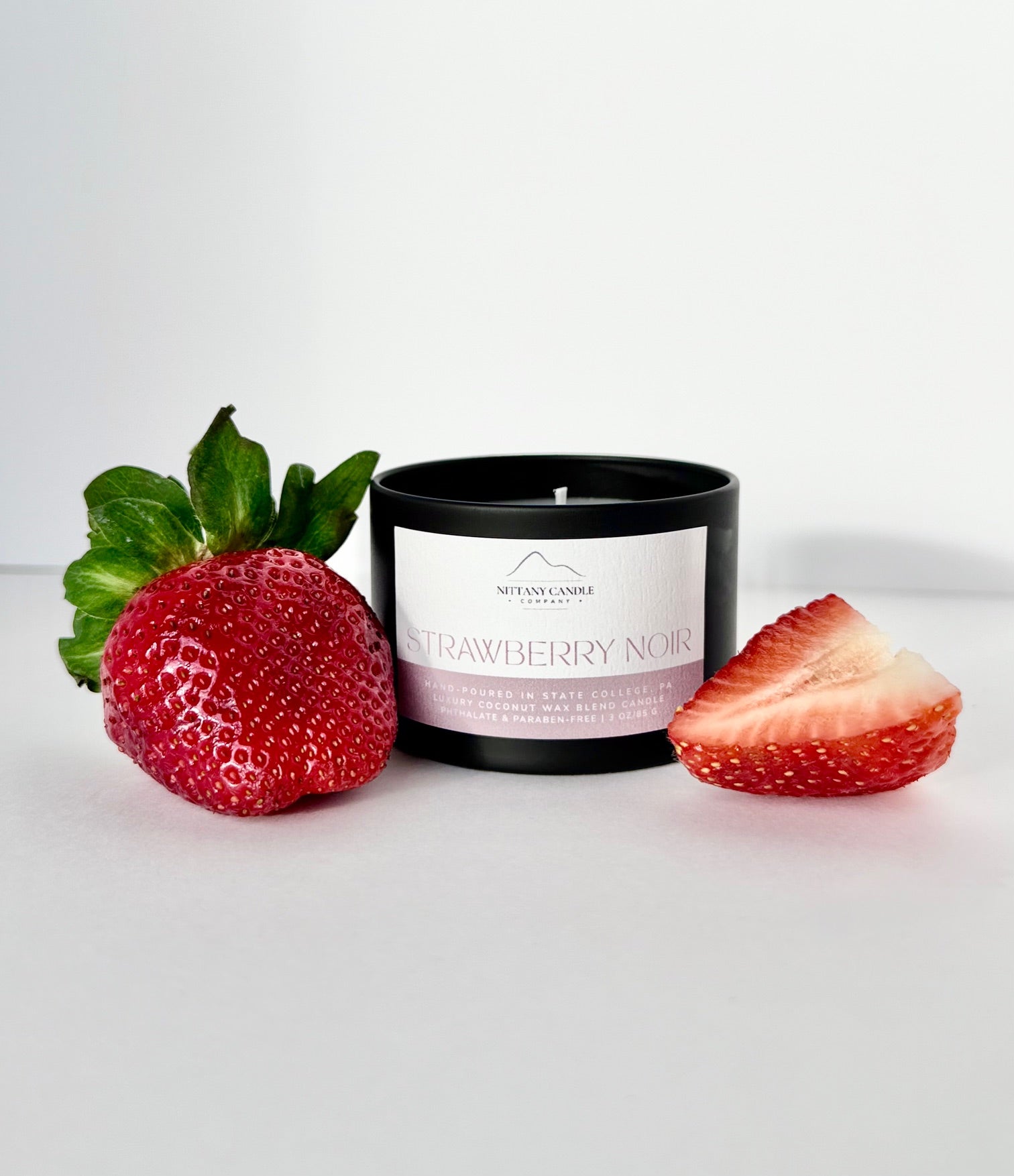 Nittany Candle Company candle labeled 'Strawberry Noir' with a whole and sliced strawberry on a white background