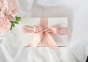 Gift box with a pink ribbon on a white fabric background with pink flowers.