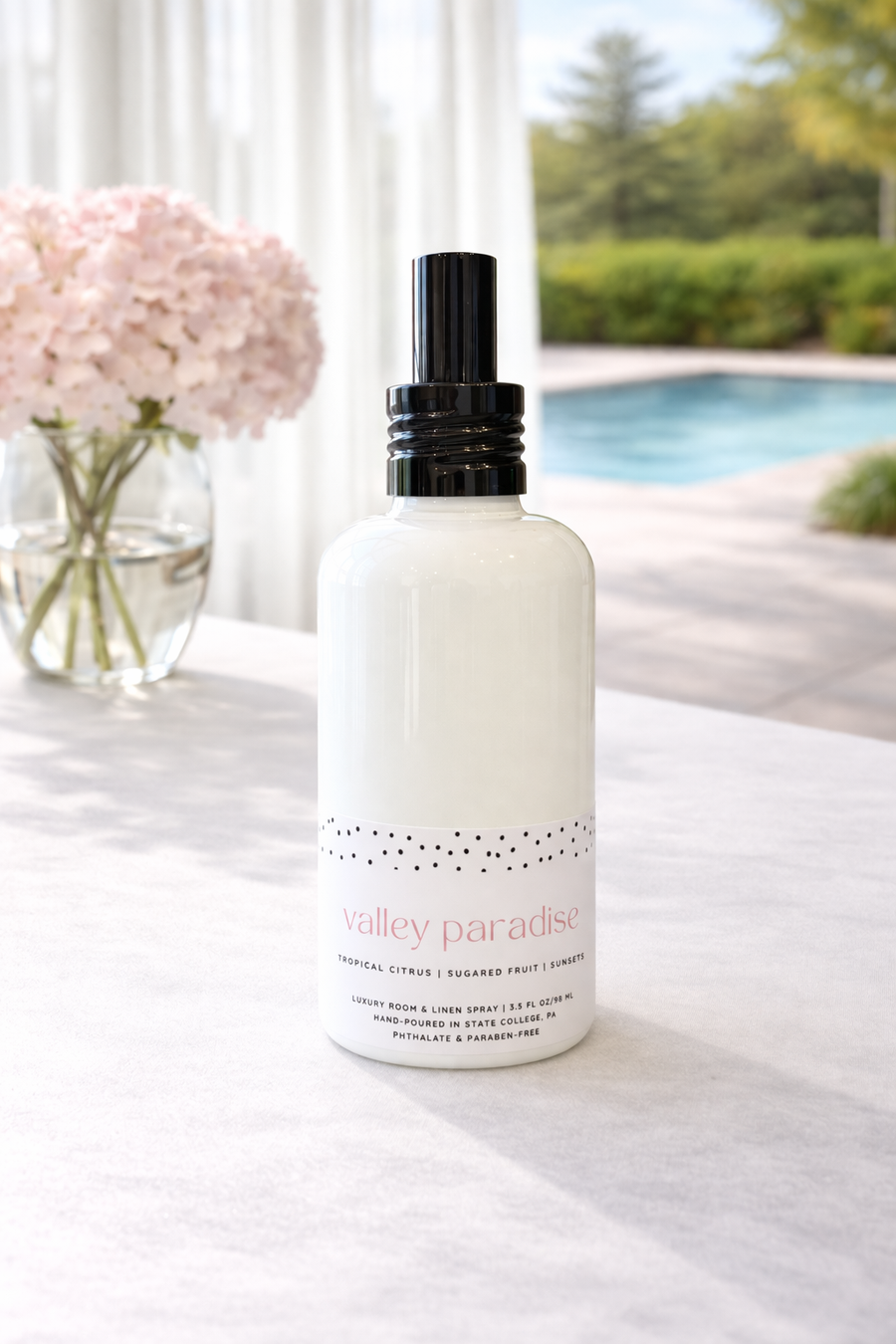 White bottle of Valley Paradise linen spray with black cap on a white surface with a blurred outdoor background