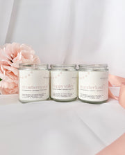 Three coconut wax candles with labels on a white surface with pink flowers in the background