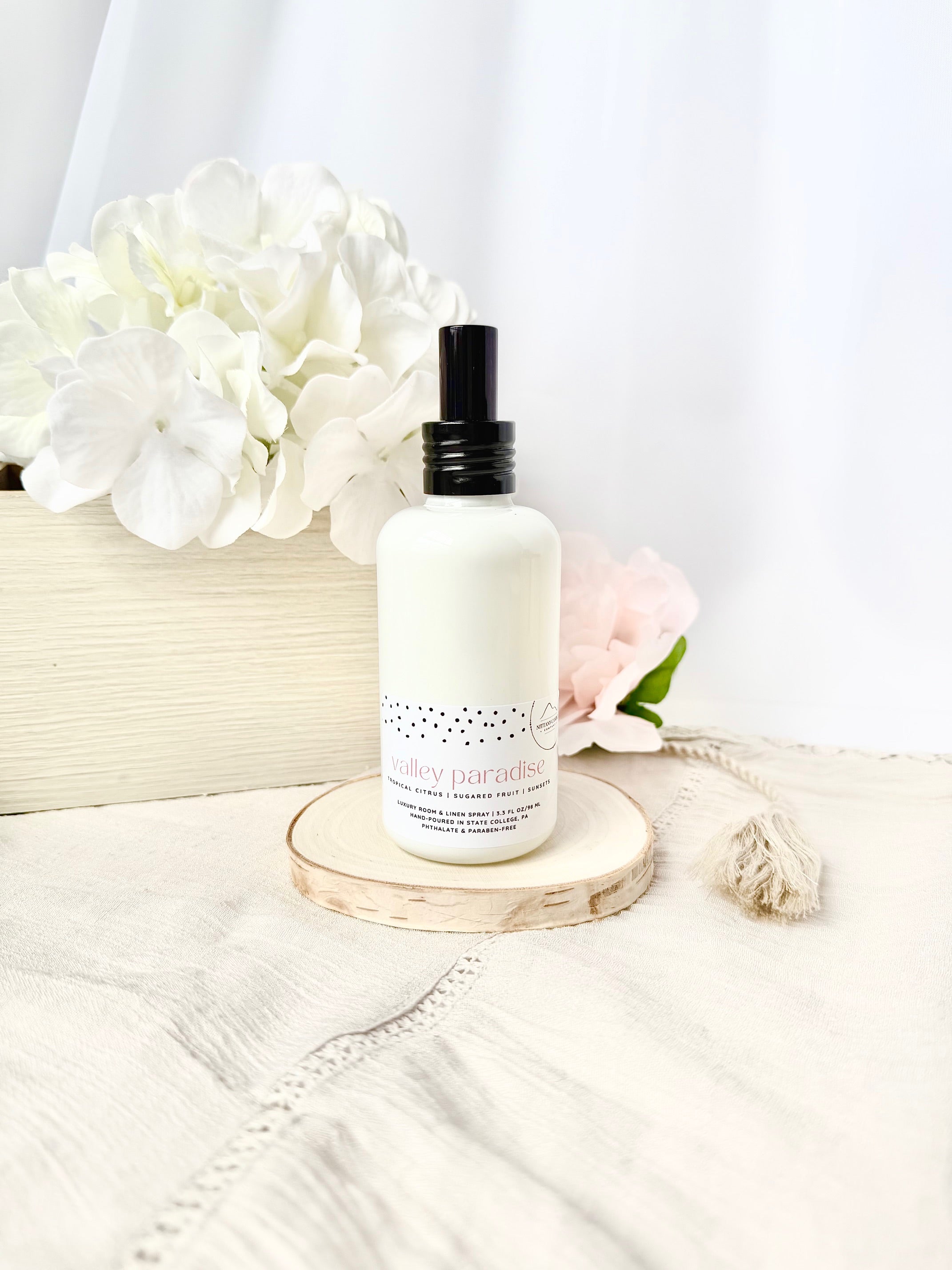 Happy Valley themed linen and room spray bottle on a wooden coaster with flowers in the background