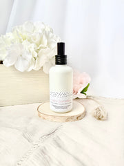 Happy Valley themed linen and room spray bottle on a wooden coaster with flowers in the background